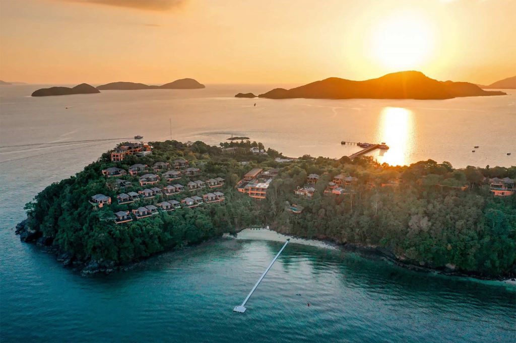 Bird's eye view of a island resort at sunset with islands in the backdrop.