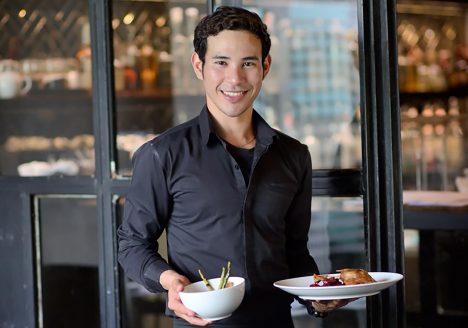 A smiling waiter carries plates of Thai food at the Eat Me restaurant in Bangkok, Thailand