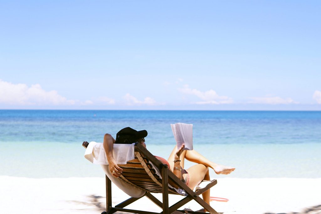 A woman relaxing on a beach in Thailand with a book in hand. 