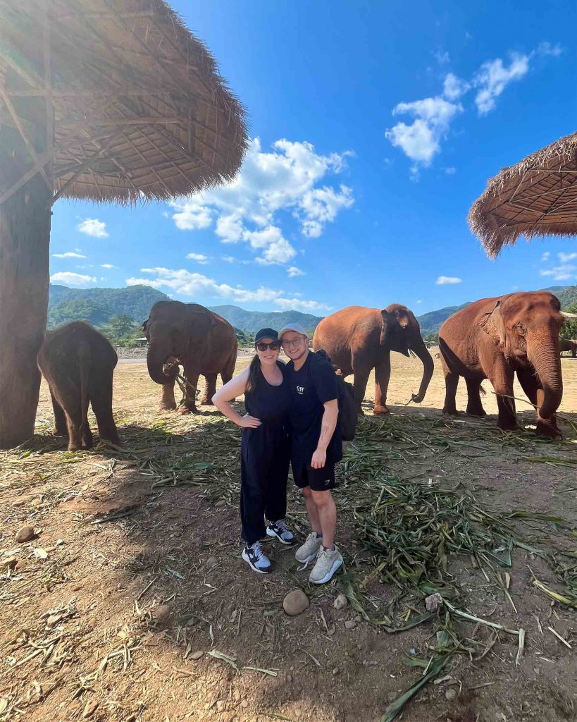 Ilana and Ren stand before a small herd of majestic elephants. Elephant interactions are some of the best queer-friendly activities in Thailand.