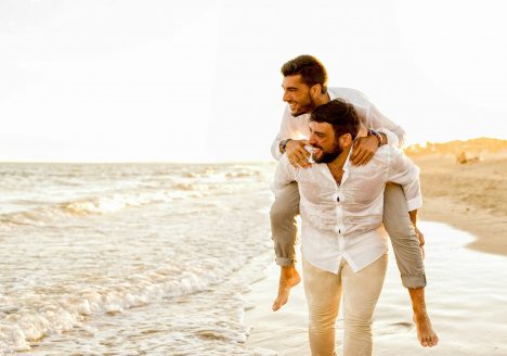 A gay man piggybacking his lover on a beach.
