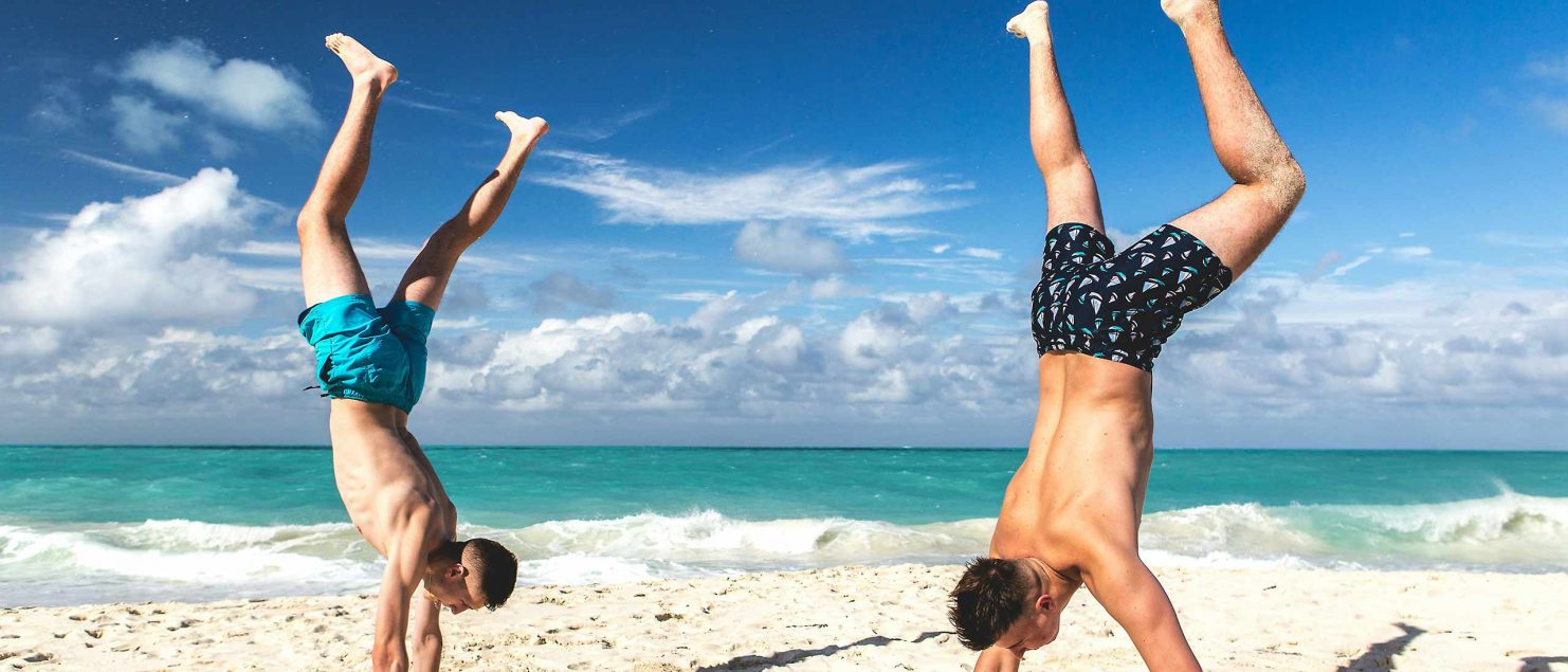 Two gay travellers doing handstands on a pristine beach in Koh Samet.