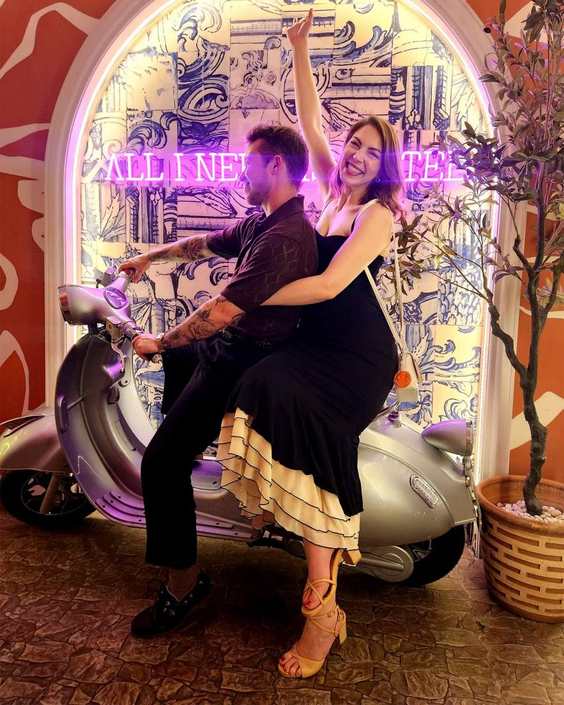 A queer couple pose in front of a wall with neon pink writing at Pastel bar. It's a must-visit for those spending one day in Bangkok.