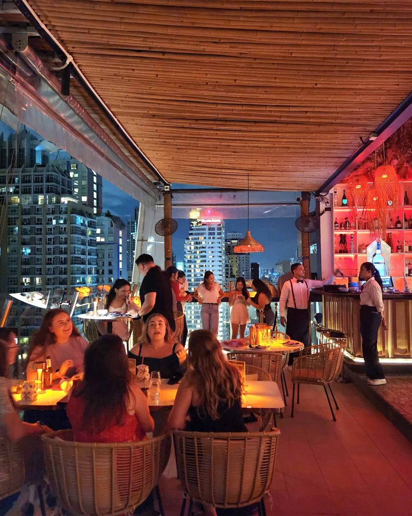 Swanky interiors of Pastel rooftop bar with the city visible behind diners.