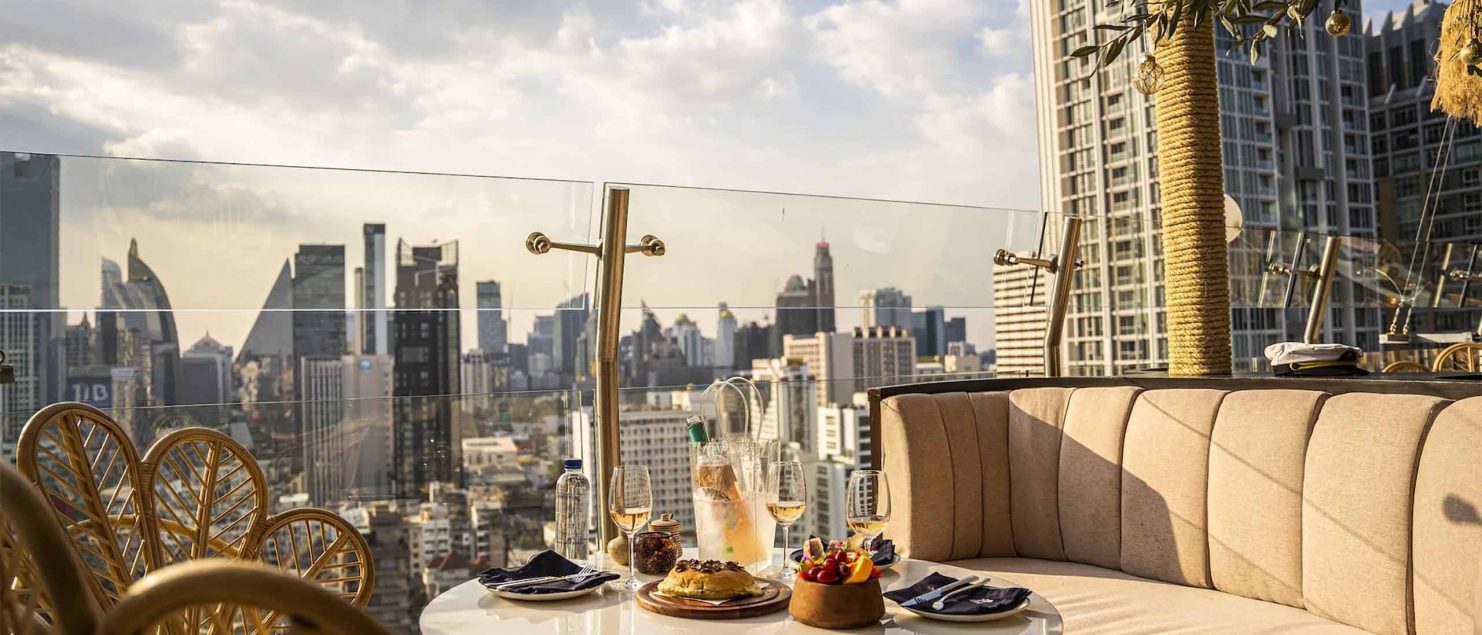 A terrace with drinks on a table and views of Bangkok during golden hour.