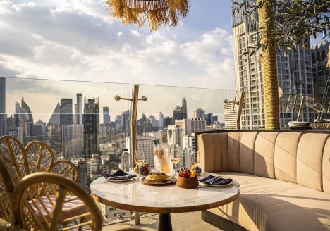 A terrace with drinks on a table and views of Bangkok during golden hour.