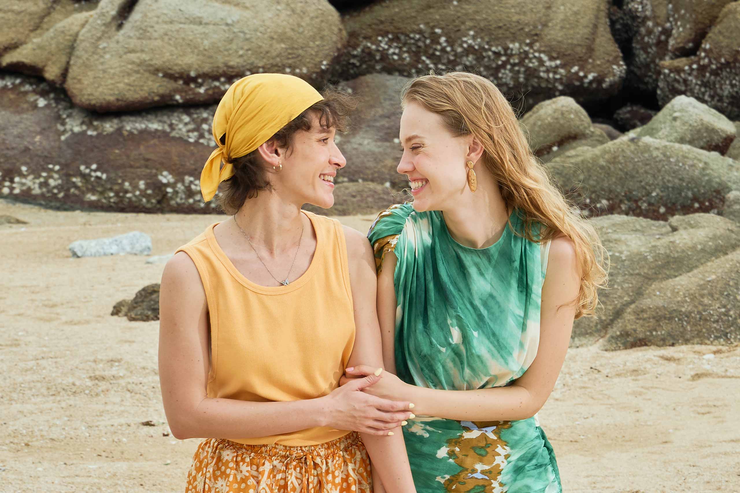 Two women hold hands on a beach in Thailand