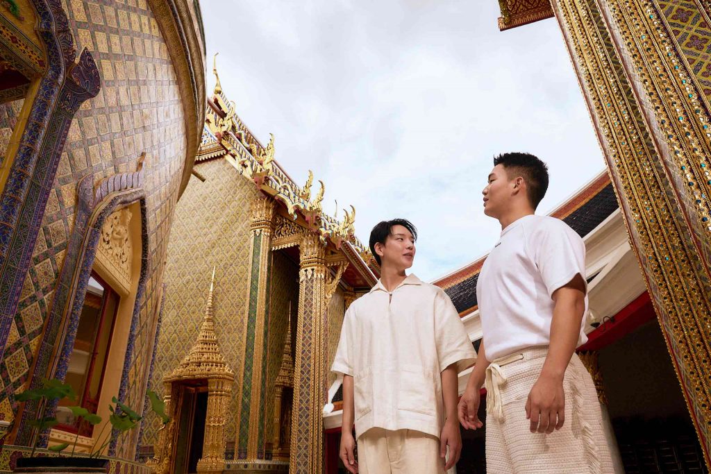 Two Asian men walk through golden buildings of a Thai Wat