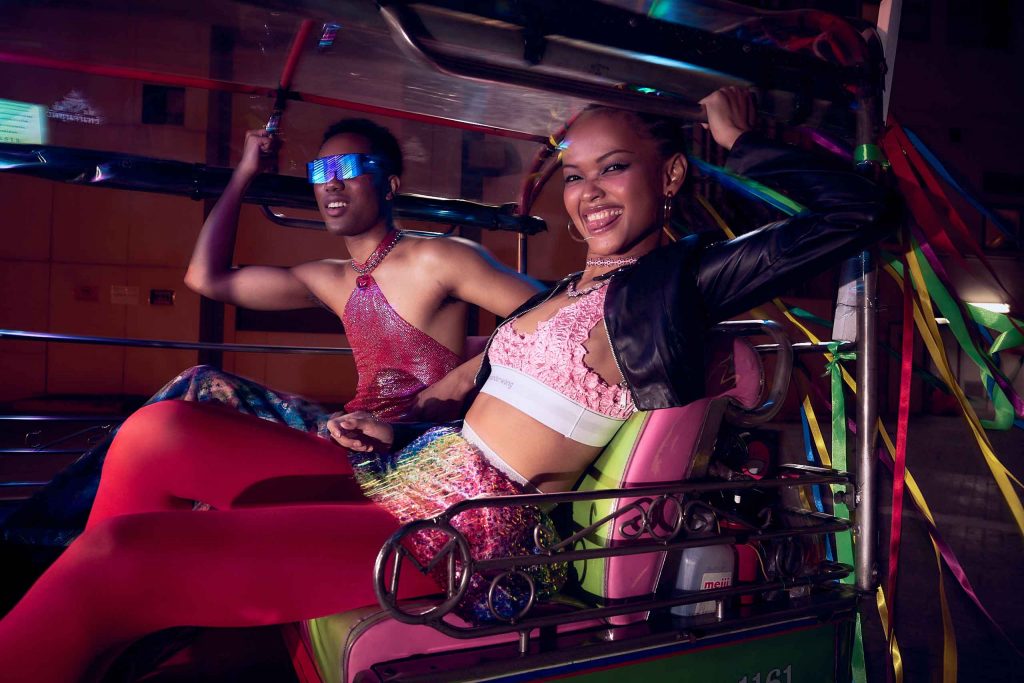 Two young people in clubwear ride on the back of a tuk-tuk in Thailand