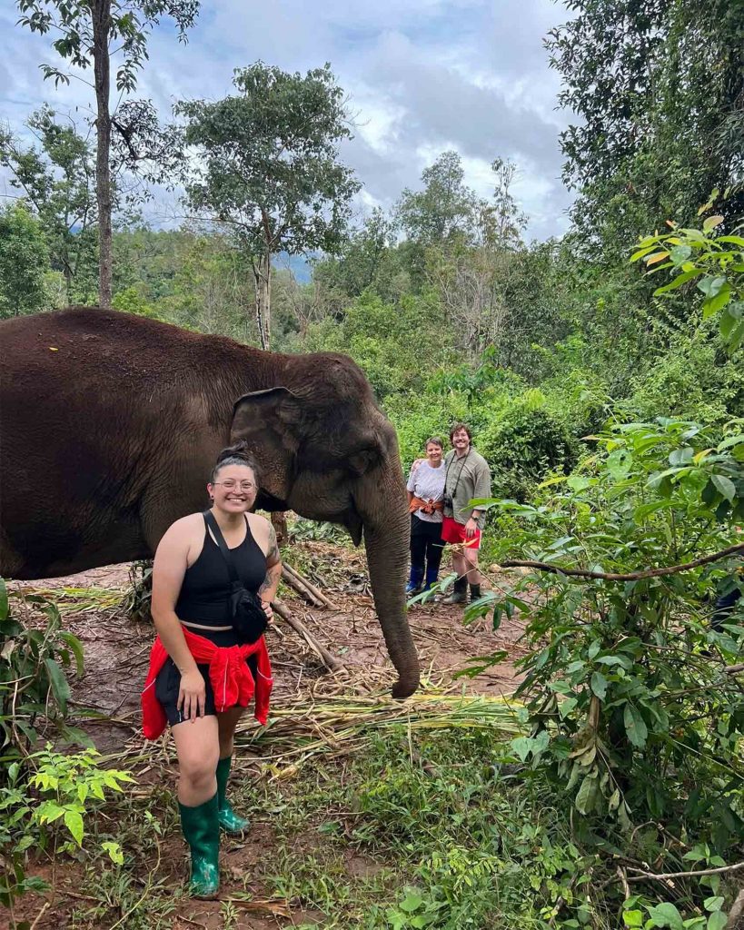 Travellers posing beside a Thai elephant in a jungle.