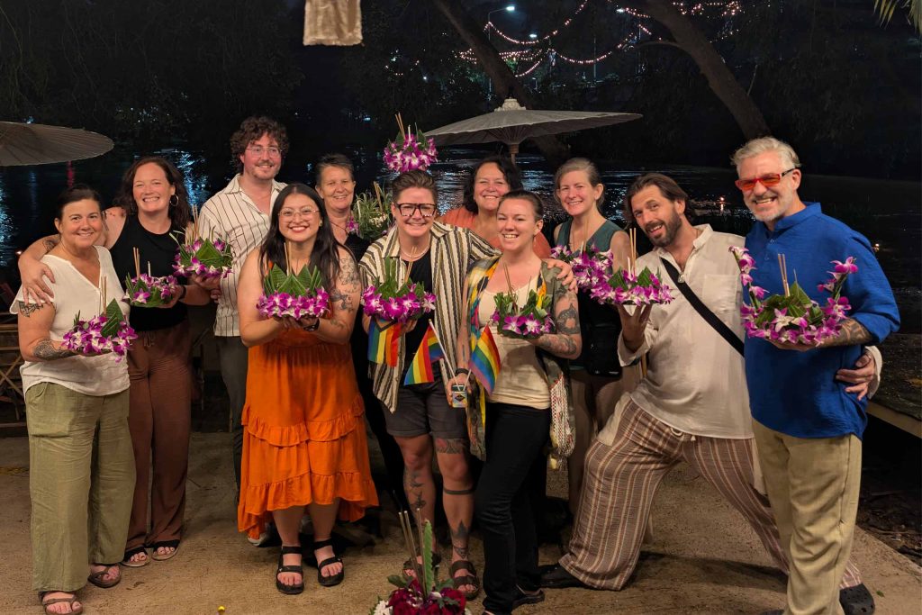 A group of queer travellers posing for a photo outside a restaurant at night.