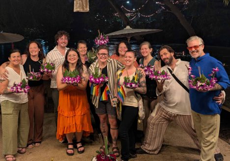 A group of queer travellers posing for a photo outside a restaurant at night.