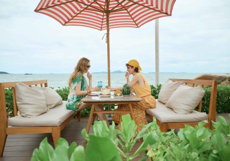 Two women sit and have breakfast by the sea