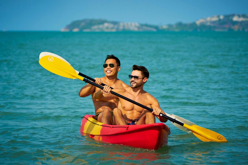 Two topless men paddle a red kayak