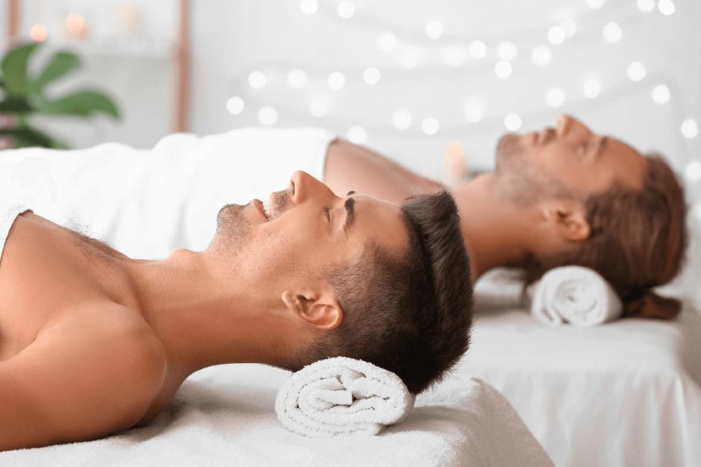 Two men lie back on a massage tables in a spa