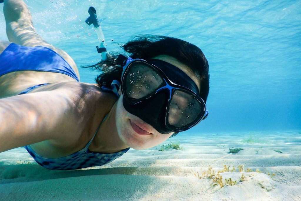 A close up of a woman snorkelling in clear waters.