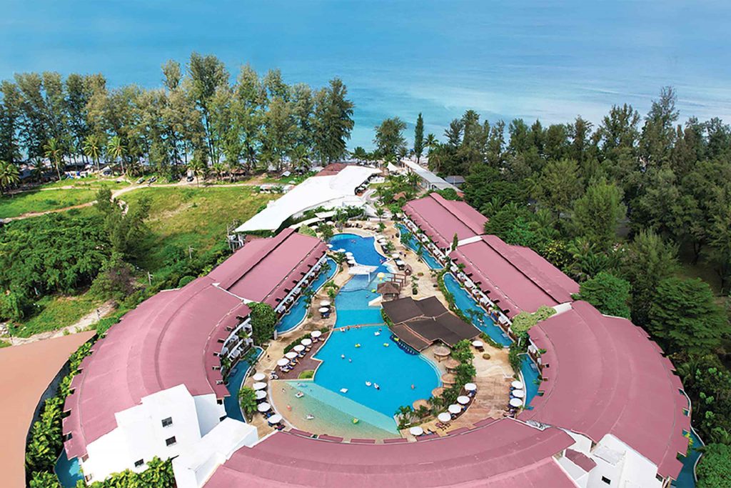 A horseshoe-shaped resort from above. A pool sits at the centre, and the coast is in the distance.