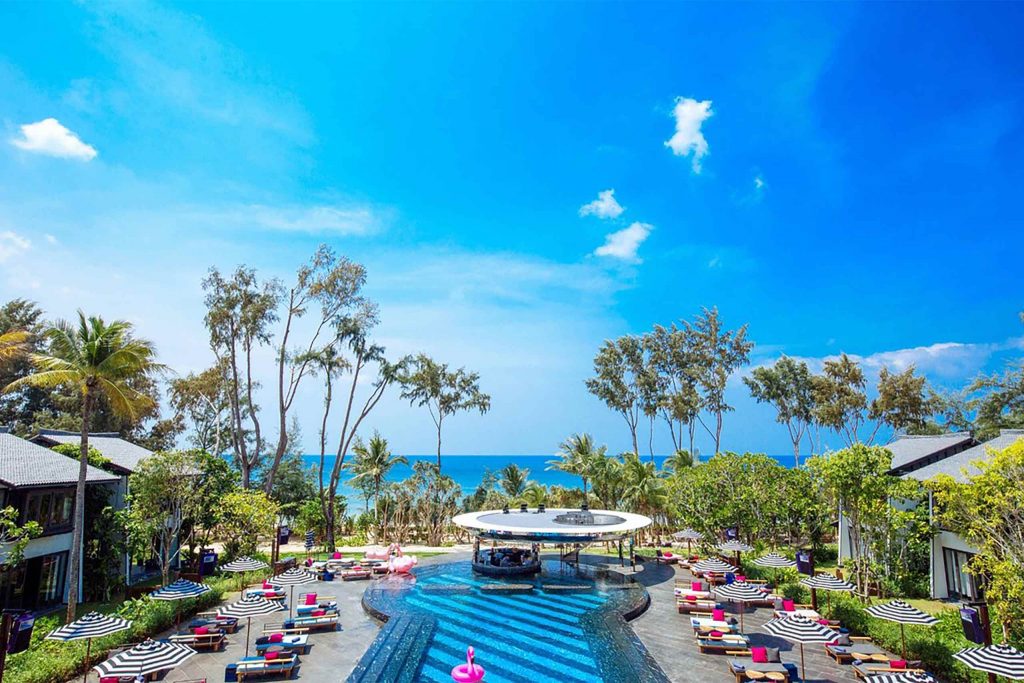 A resort with a pool and palm trees at its centre. The resort looks out onto the ocean.