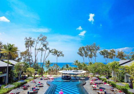 A resort with a pool and palm trees at its centre. The resort looks out onto the ocean.