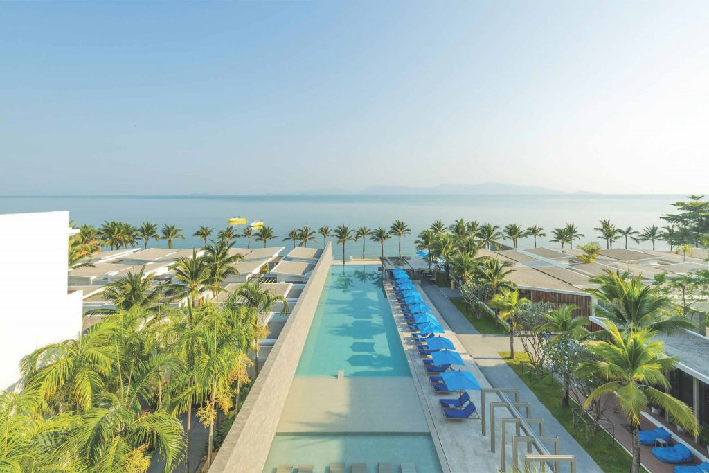 A blue pool surrounded by greenery. The ocean and sky touch in the backdrop.