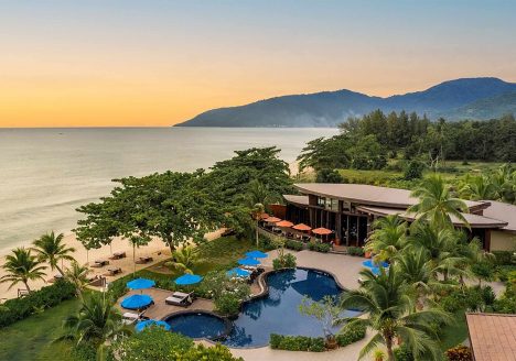 A resort pressed against the ocean at sunset. Silhouettes of hills are in the distance.