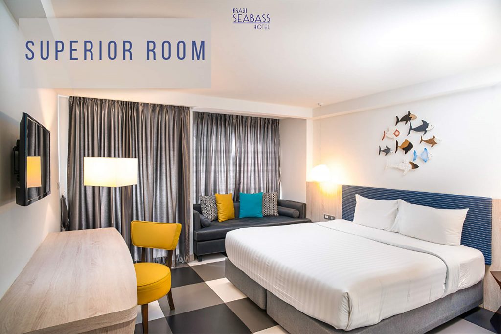 A bedroom with white walls. A grey bed is against the wall and colourful elements are dotted about the room.