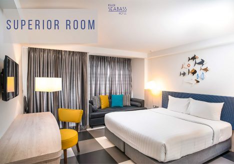 A bedroom with white walls. A grey bed is against the wall and colourful elements are dotted about the room.