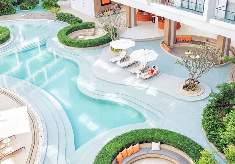 Overhead view of a resort pool with a woman lounging beside it.