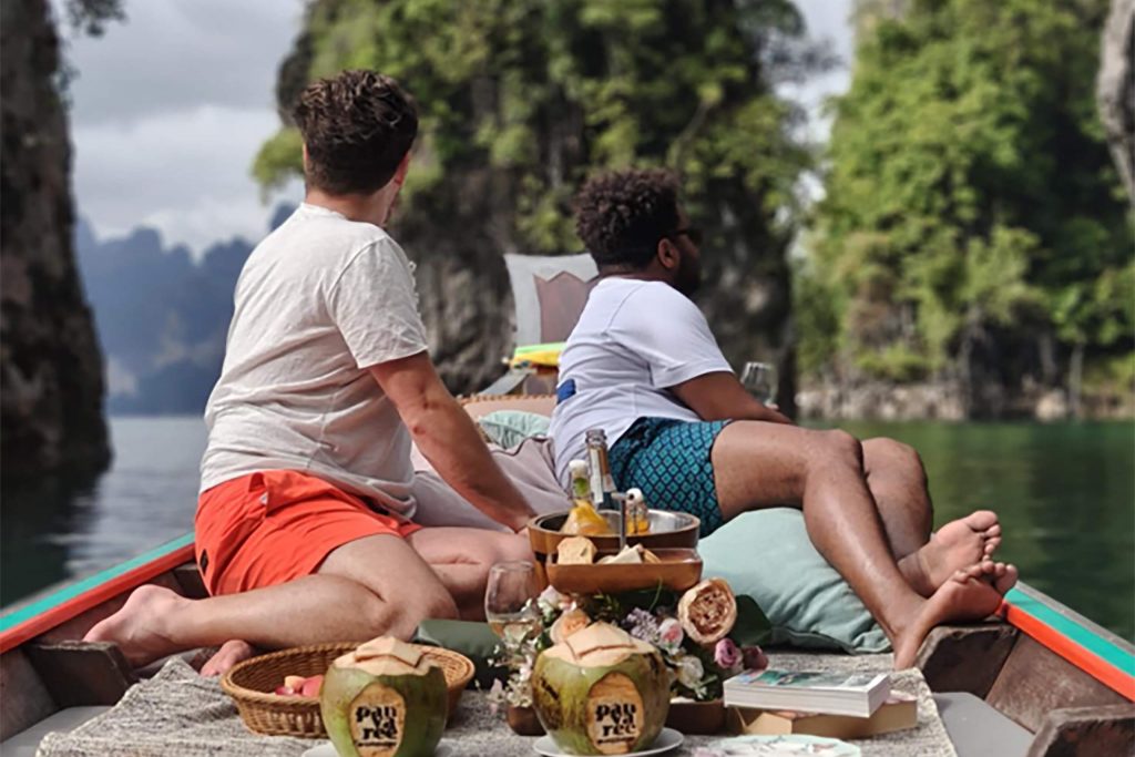 An interracial gay couple on a boat together facing outwards.