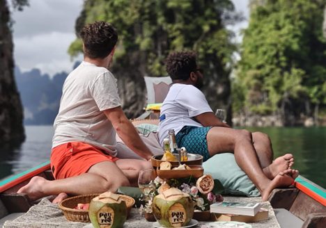 An interracial gay couple on a boat together facing outwards.