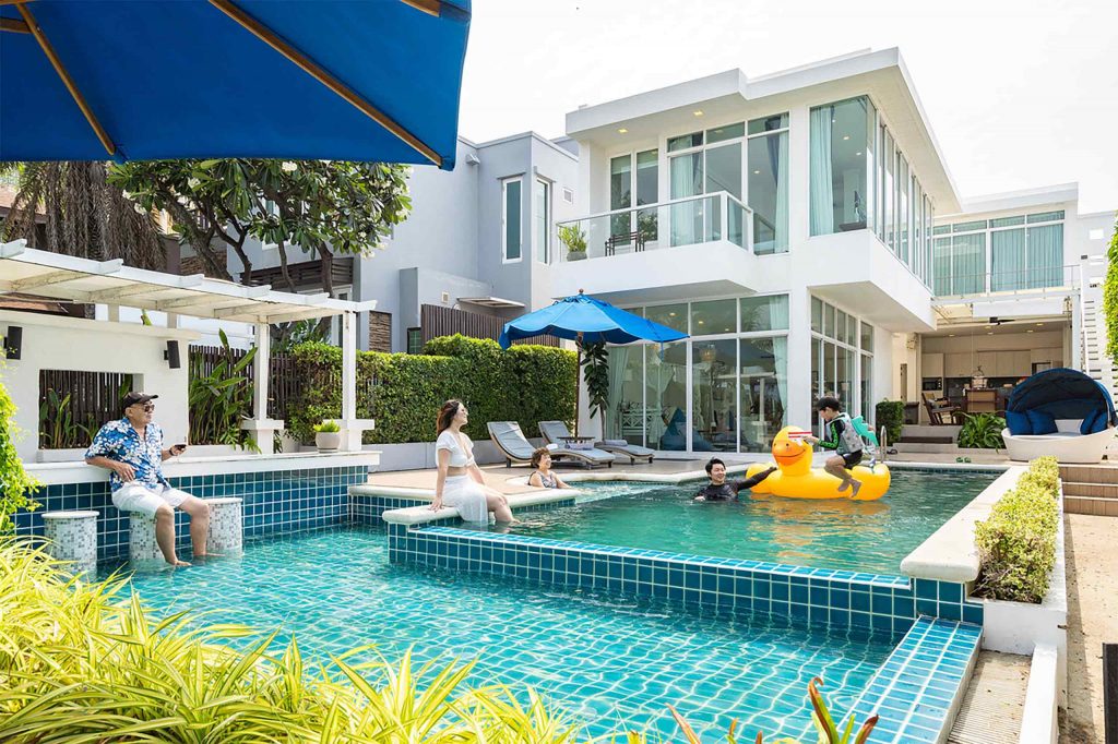 A white modern villa behind a pool with a family relaxing in it.