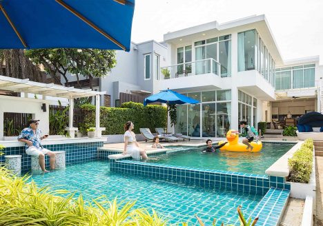A white modern villa behind a pool with a family relaxing in it.
