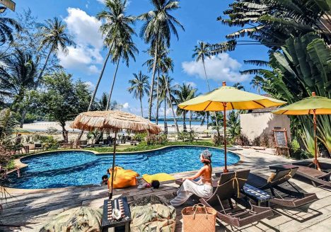 A pool at a resort with a woman relaxing beside it.