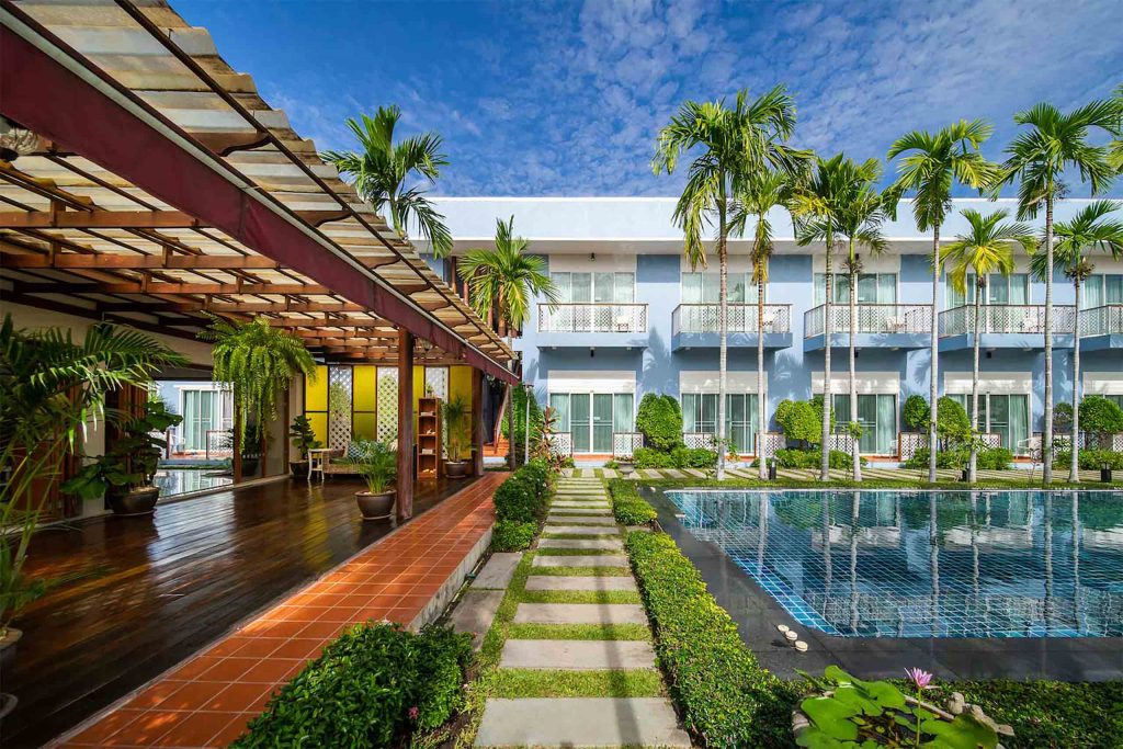 A hotel complex with a pool on the right and a teakwood public space on the left.