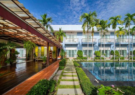 A hotel complex with a pool on the right and a teakwood public space on the left.