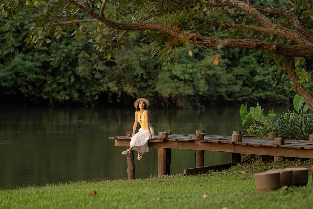 A female traveller sat by a river, surrounded by trees.