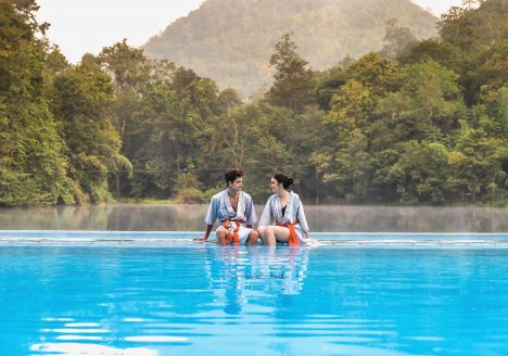 Two travellers sitting poolside with a forest in the background.