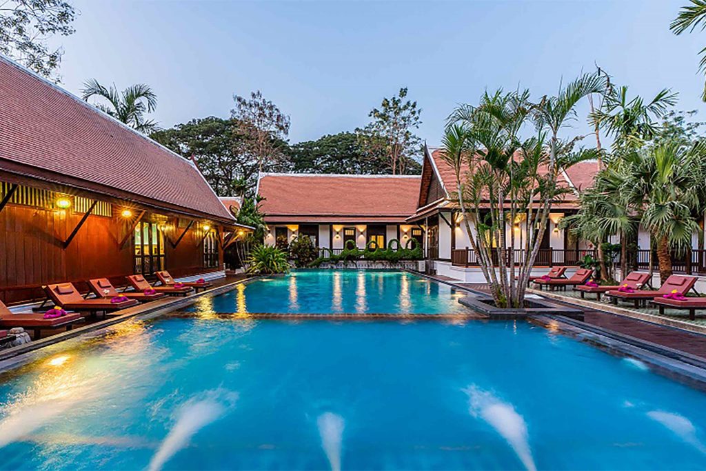 A bright blue pool with a traditional Thai building surrounding.
