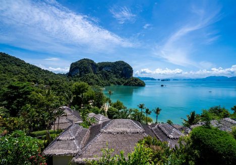 Thatched-roof villas dotting a forest near the ocean.