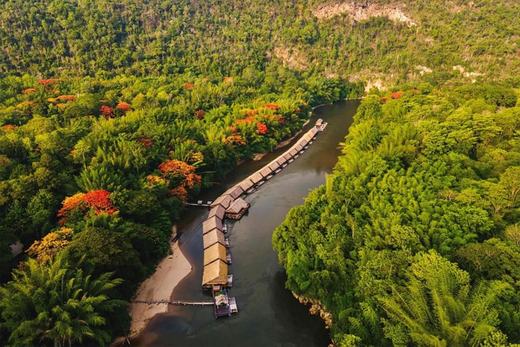 A row of floating bungalows on a river, surrounded by forest.