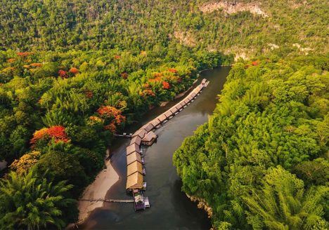 A row of floating bungalows on a river, surrounded by forest.