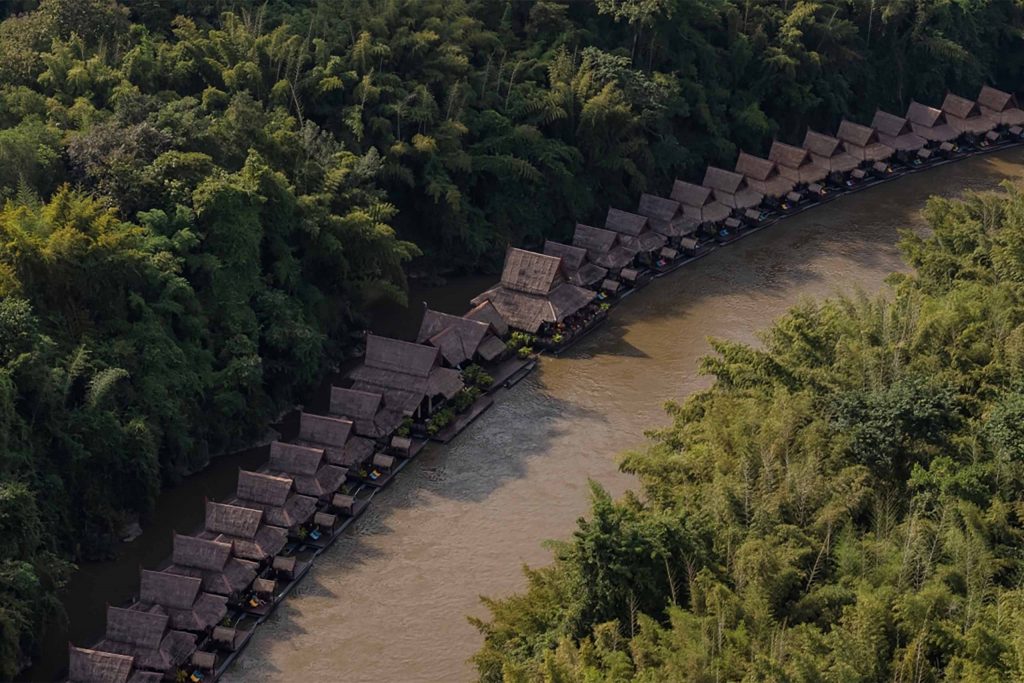 A row of bungalows stretches across a river bend. The river is surrounded by forest.