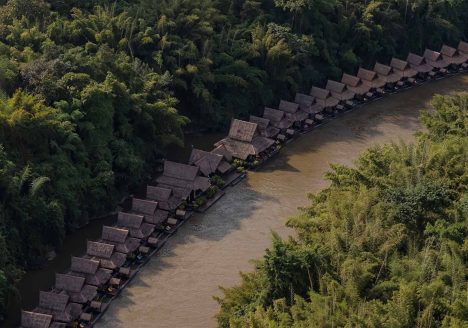 A row of bungalows stretches across a river bend. The river is surrounded by forest.