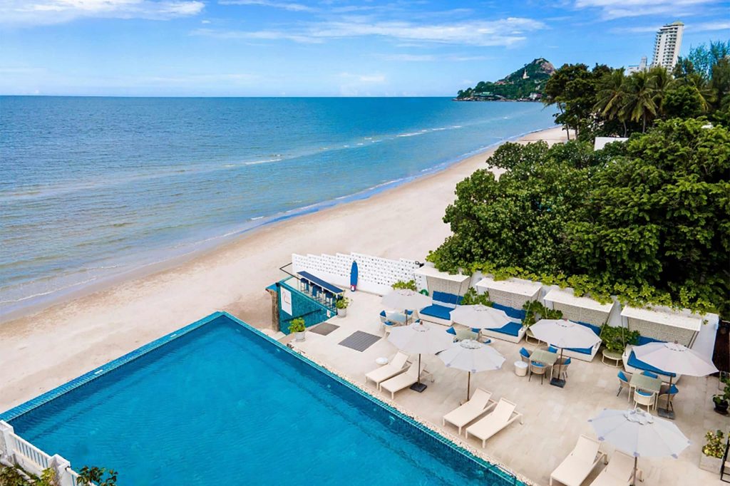 An overhead shot of a resort pool area with a beach and ocean directly next to it.