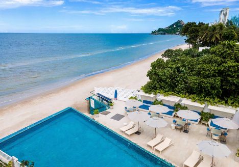 An overhead shot of a resort pool area with a beach and ocean directly next to it.