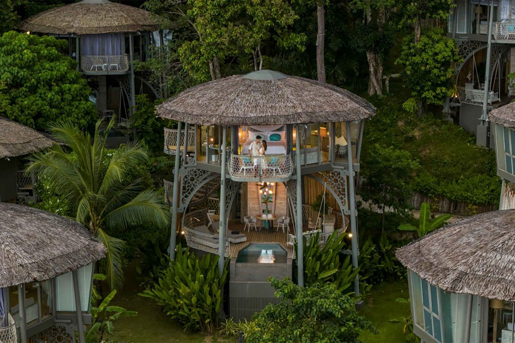 Charming stilted villas standing tall in a forest at twilight with their interiors lit by lanterns.