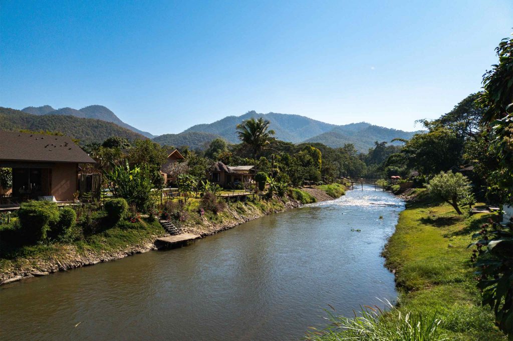 A peaceful river winding through a lush valley surrounded by forested mountains in Northern Thailand.