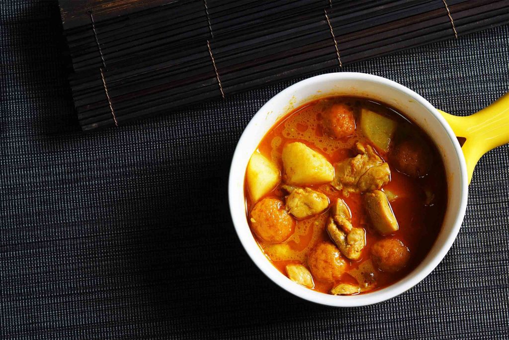 A bowl of rich curry with chicken, potatoes and peanuts in a bright yellow dish. A comforting Thai Food.