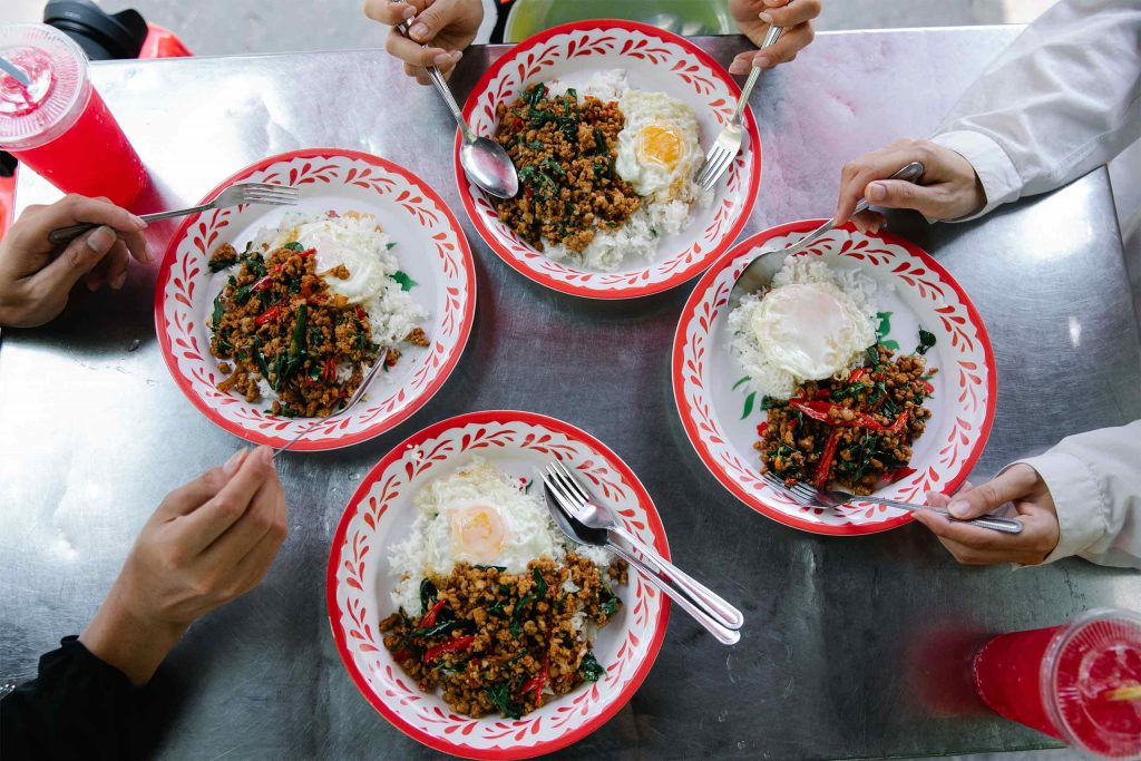 Four plates of basil stir-fry with fried eggs served around a shared table. A popular Thai Food for everyday dining.