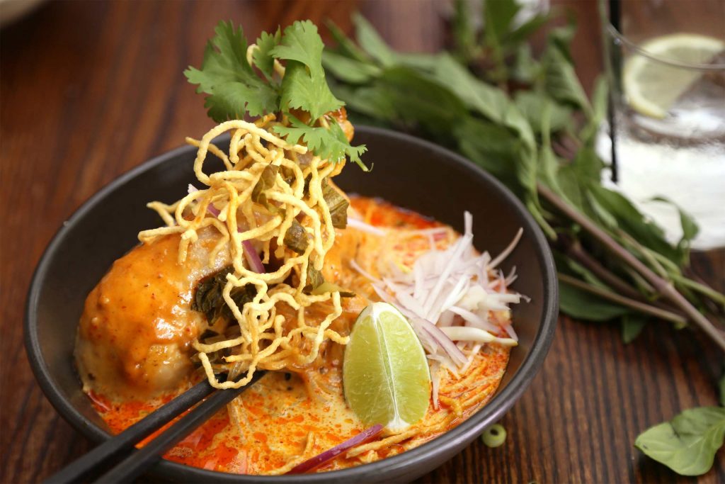 A bowl of creamy khao soi topped with crispy noodles, herbs and a wedge of lime. An essential Thai Food.